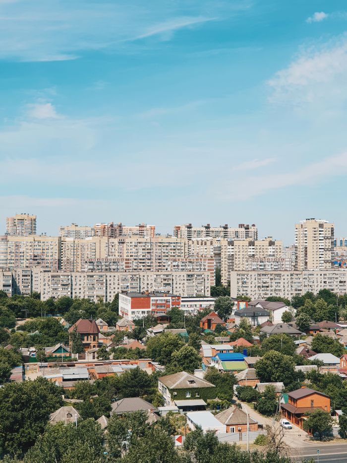 impact-img A vibrant cityscape featuring tall residential buildings and lush greenery under a bright blue sky.