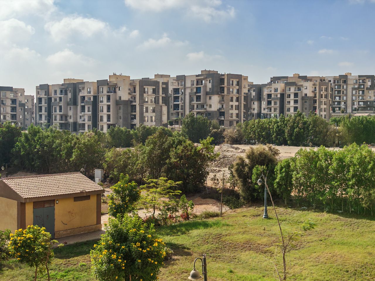 hero-about View of modern apartment buildings surrounded by greenery under a clear sky.